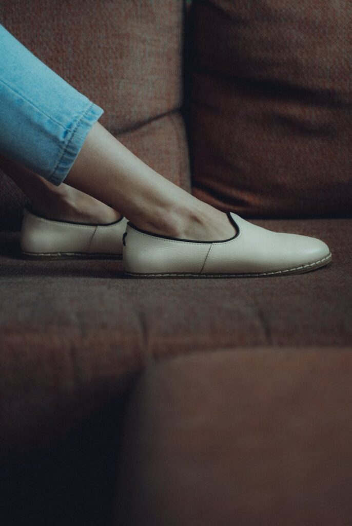 Close-up shot of stylish beige flats and jeans on a vintage couch, emphasizing casual fashion.