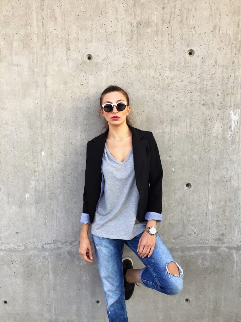 A young woman in stylish casual attire poses against a concrete wall in Thessaloniki, Greece.