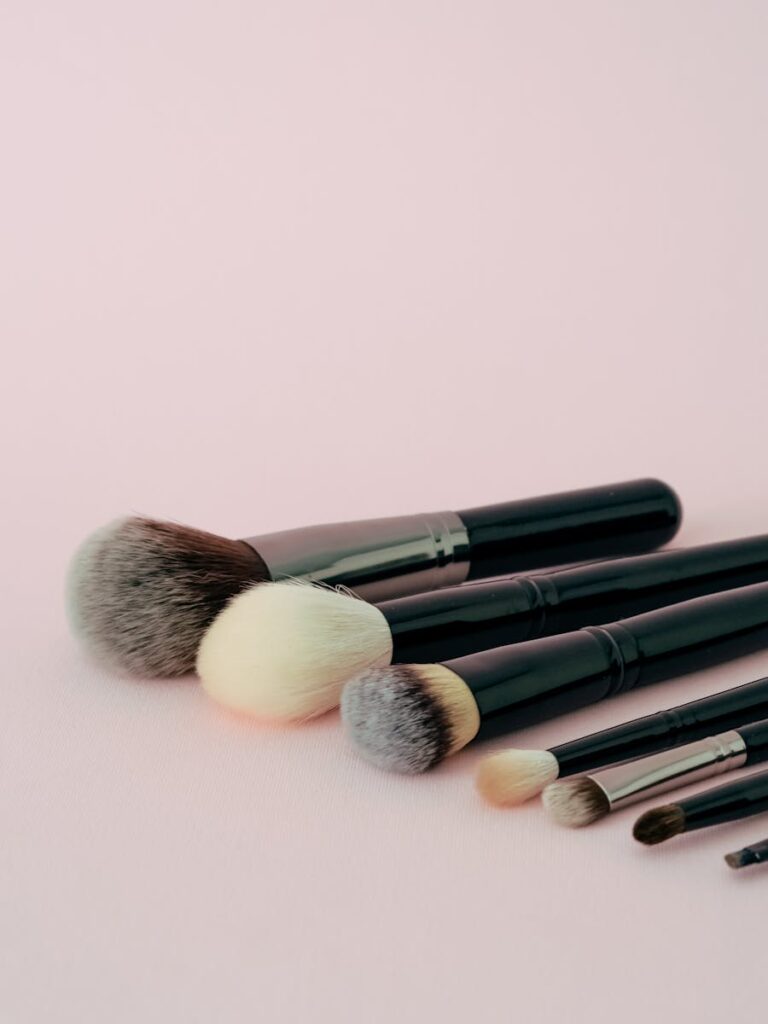 Various makeup brushes arranged on a pastel pink background for beauty and fashion themes.