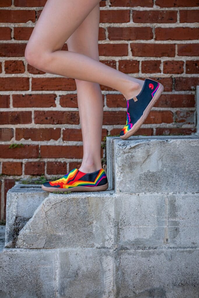 Vibrant rainbow sneakers worn by woman on concrete steps against brick wall.