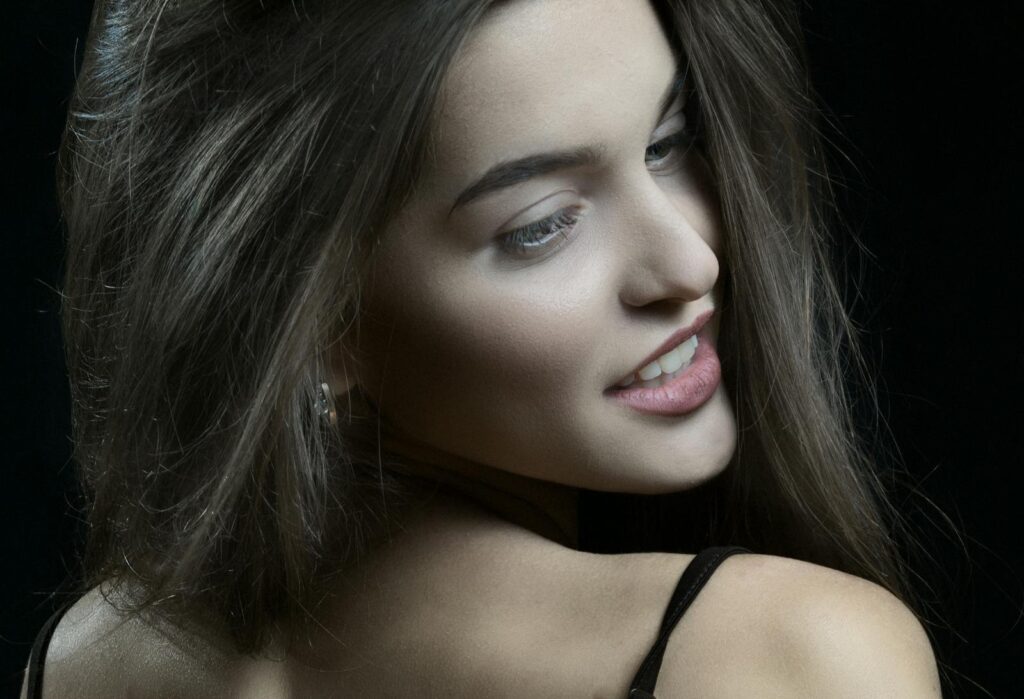 Portrait of a woman with long brown hair posing confidently against a black background.