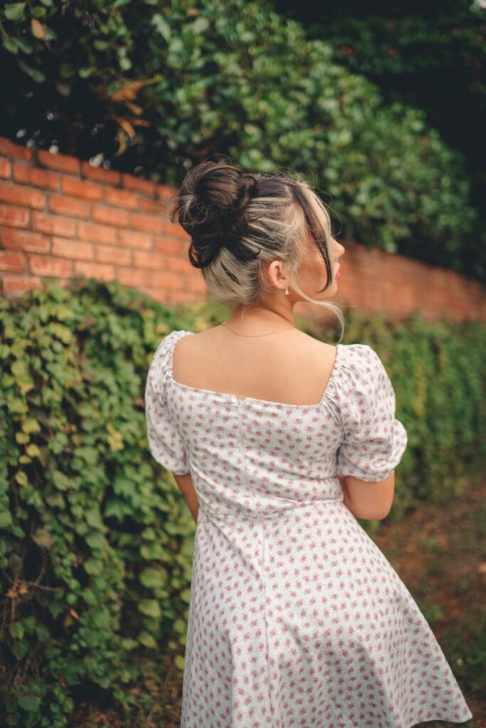 Woman in a summer polka dot dress with back view walking along a brick wall covered in ivy.
