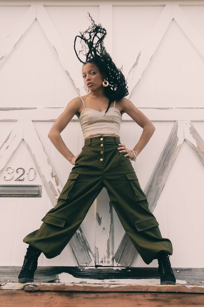 Confident woman poses in stylish pants and top, showcasing dynamic fashion in a modern urban setting.