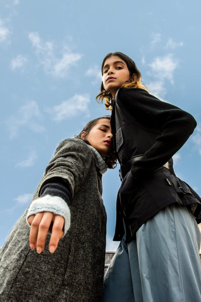Two stylish women posing confidently against a bright sky, showcasing modern fashion.