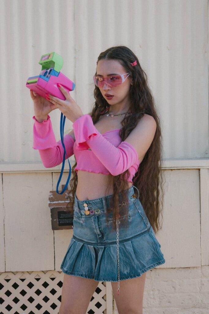 Fashionable young woman in pink outfit using a colorful vintage camera outdoors.