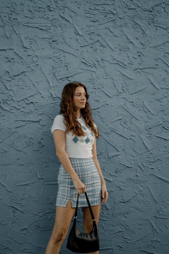 A fashionable woman stands confidently against a blue textured wall, showcasing summer style.