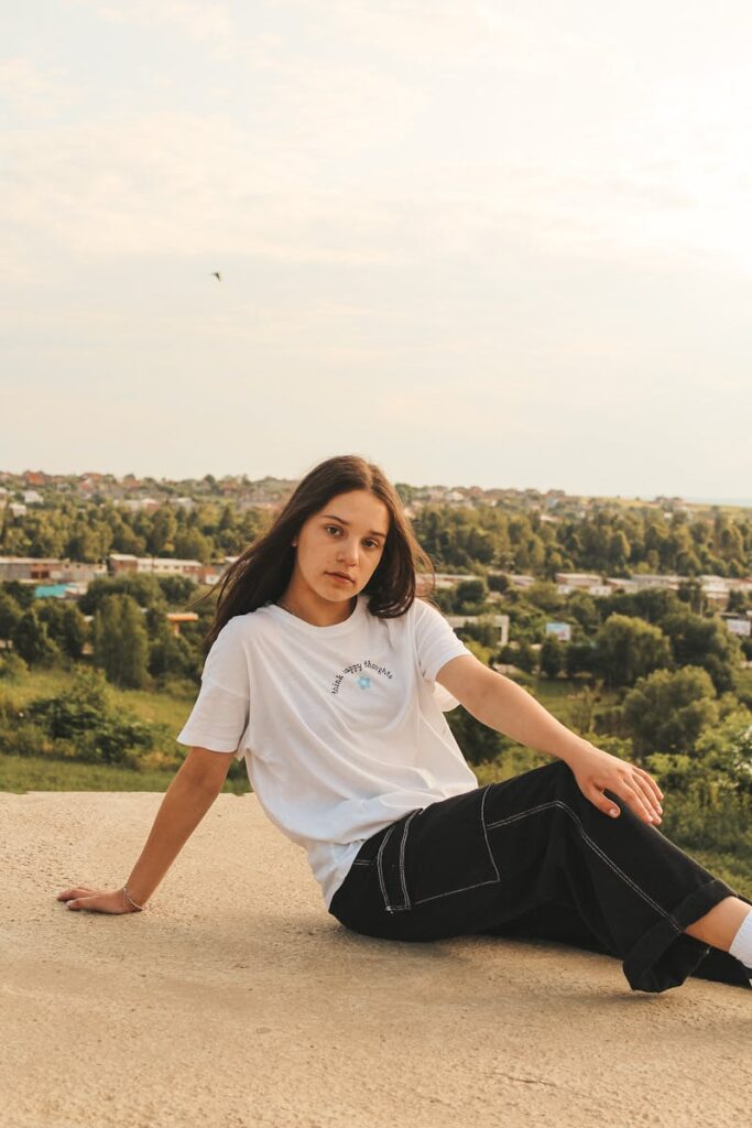 Casual young woman sitting outdoors with a cityscape view in the background.