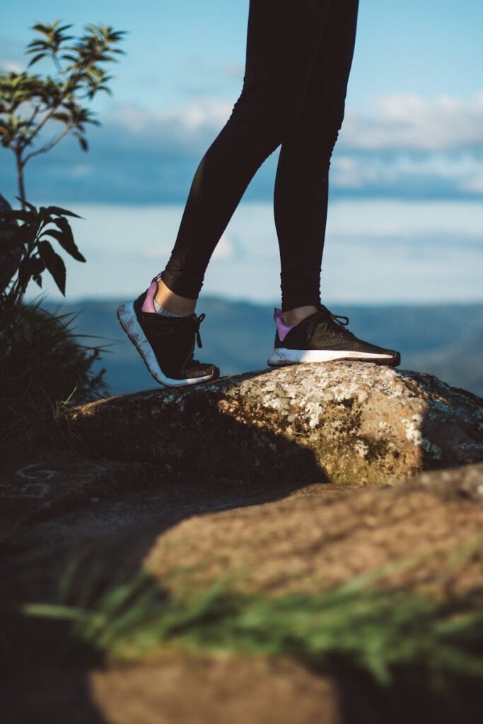 Person hiking on rocky terrain with scenic mountain view, wearing sneakers.
