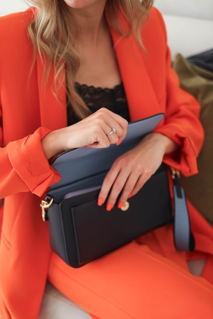 Fashionable woman in orange suit holding a stylish handbag indoors.