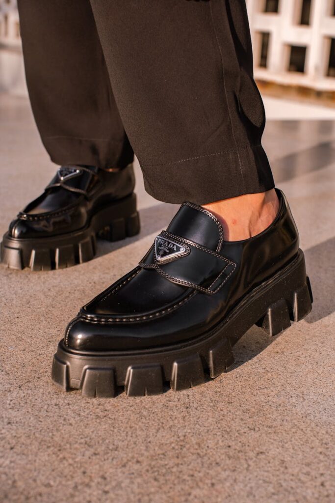Fashionable black leather loafers with chunky soles worn outdoors.
