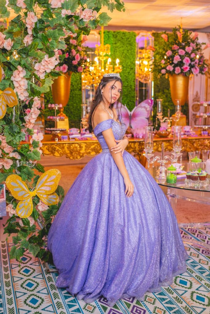 A stunning bride wearing a lavender gown poses in a lavishly decorated banquet hall filled with flowers.