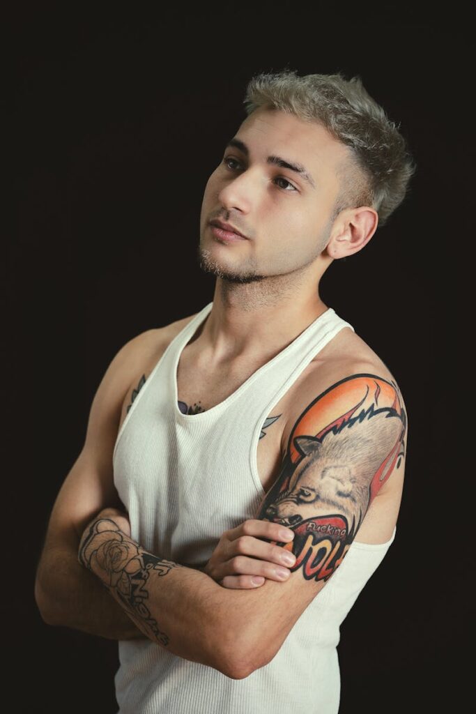 Portrait of a young man in a tank top showcasing detailed tattoos in a studio setting.