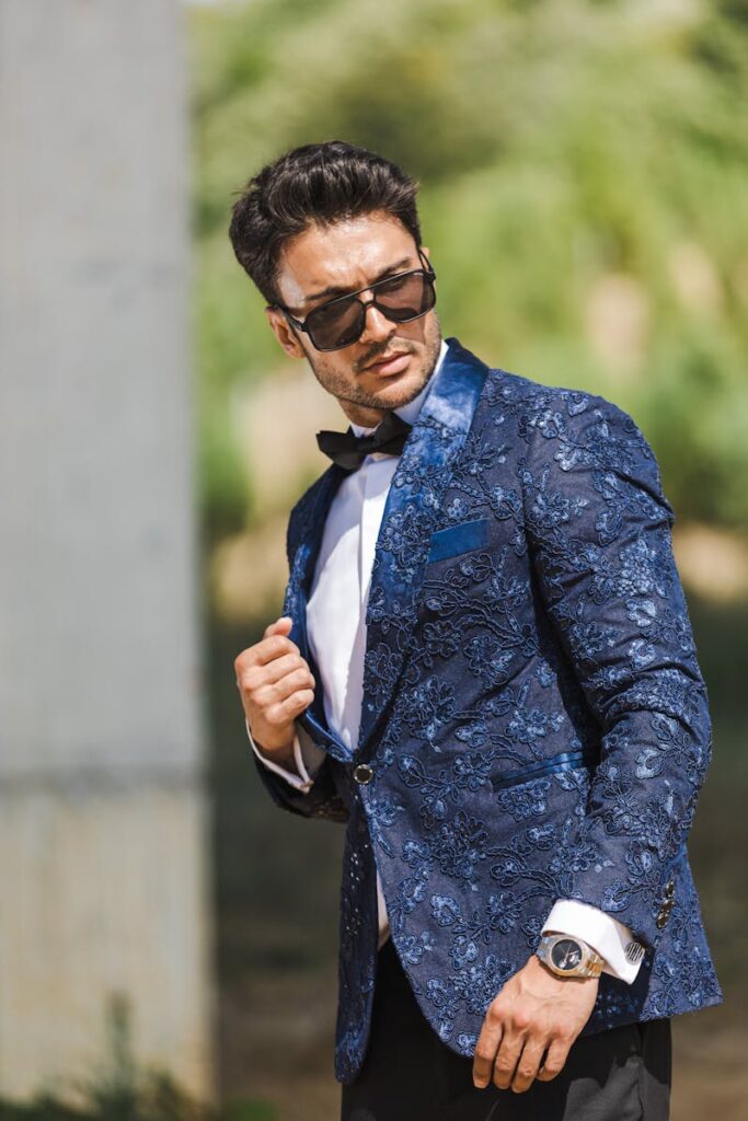 Fashionable man poses confidently in an embroidered navy tuxedo with sunglasses.