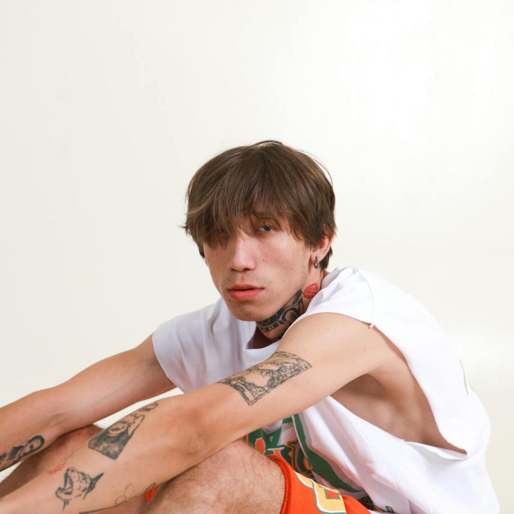 Portrait of a trendy young man with tattoos sitting casually in a studio setting.