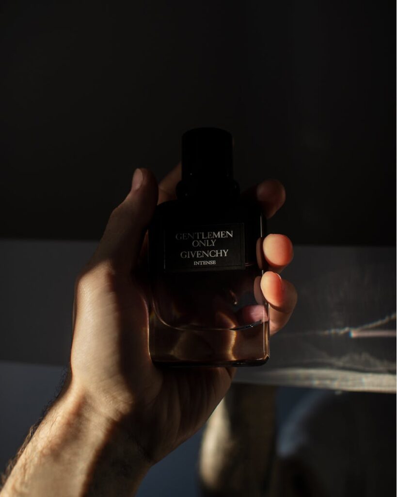 A man's hand holds a Givenchy perfume bottle with dramatic lighting.