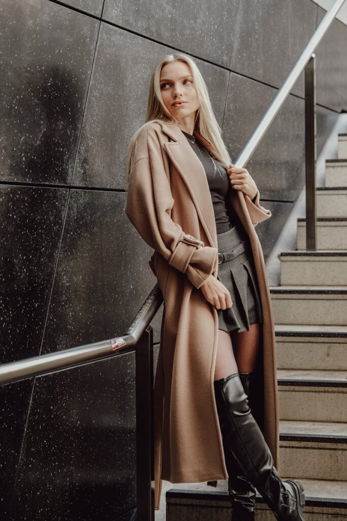 Elegant woman posing in a trench coat and knee boots on a subway staircase, embodying urban fashion.