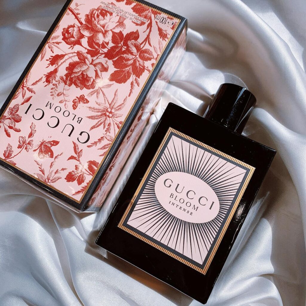 Elegant Gucci Bloom Intense perfume bottle and box on white silk fabric.