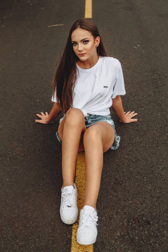 Casual fashion portrait of a young woman sitting on a road, showcasing modern street style.
