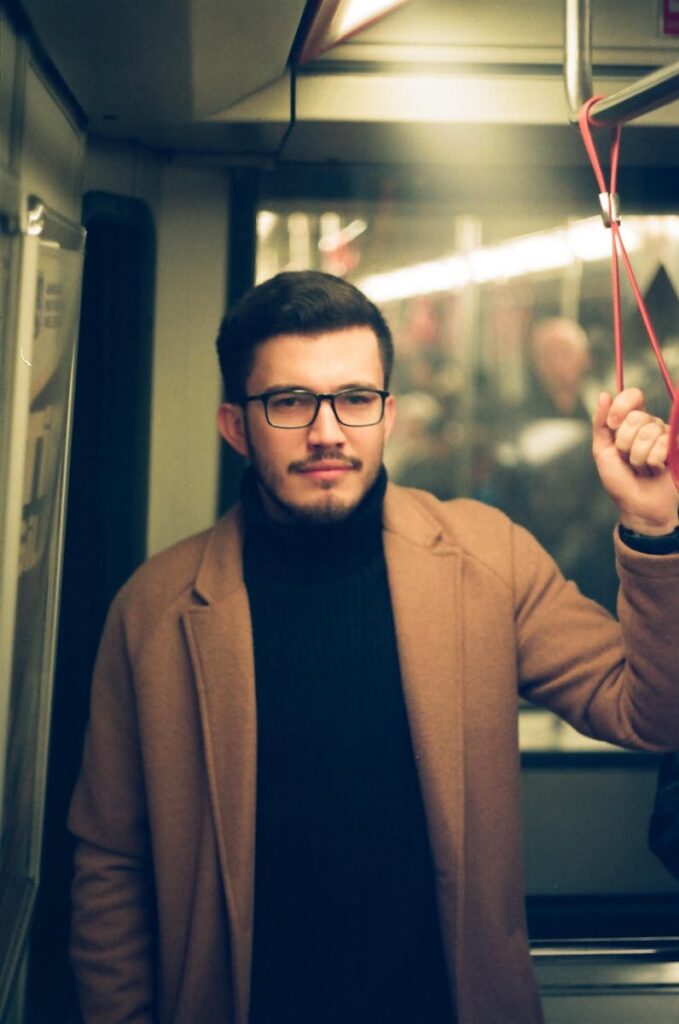 Portrait of a fashionable man in a subway holding onto a handle, showcasing urban fashion.