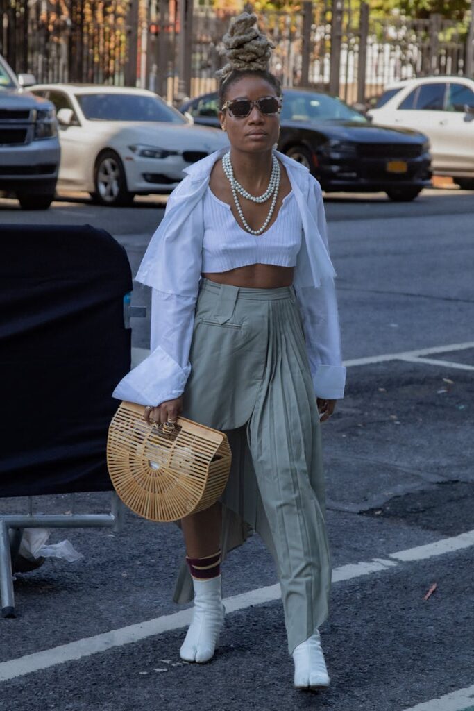 Fashionable woman in urban New York City street wearing stylish attire with bamboo basket bag.