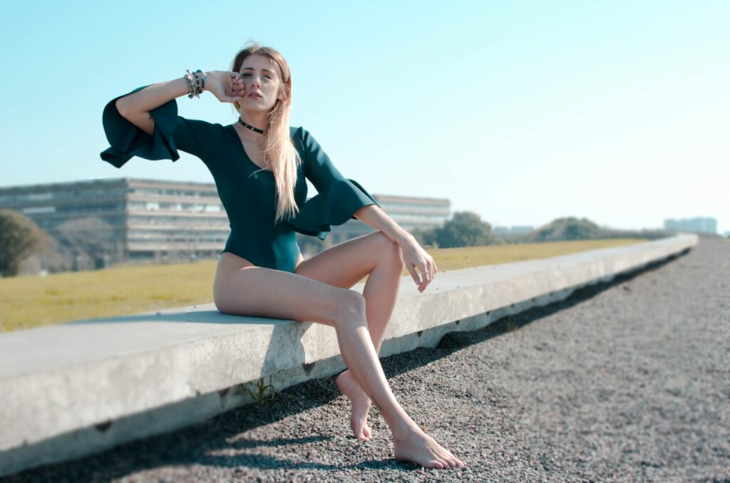 A stylish woman poses outdoors in a green bodysuit, enjoying a sunny day.