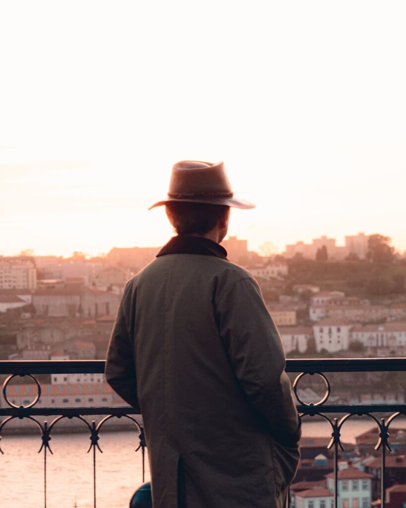 A man in a hat and trench coat overlooks Porto, Portugal at sunset, capturing urban travel vibes.