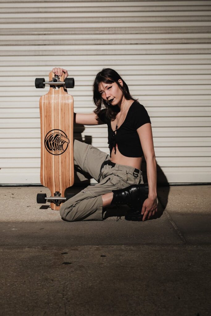 Woman in cargo pants holding a longboard in an urban garage setting.