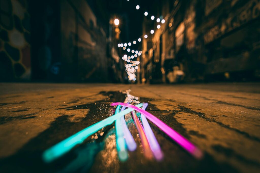 Colorful glowsticks illuminate a wet urban alley at night, reflecting bokeh lights in Knoxville.