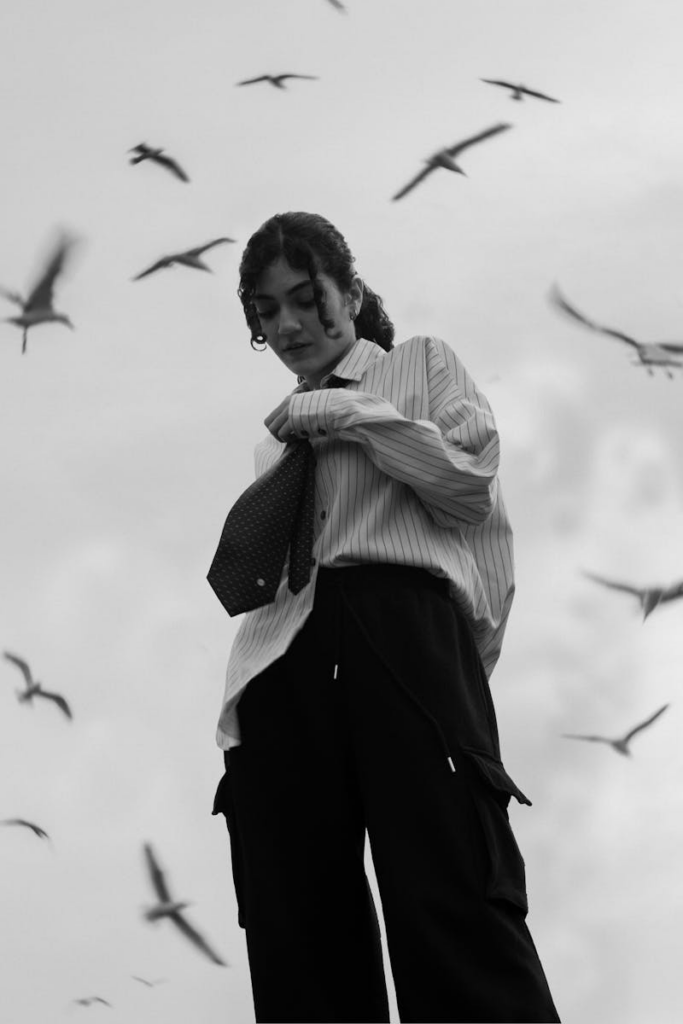 Black and white photo of a woman adjusting her tie with seagulls in the sky above İstanbul.