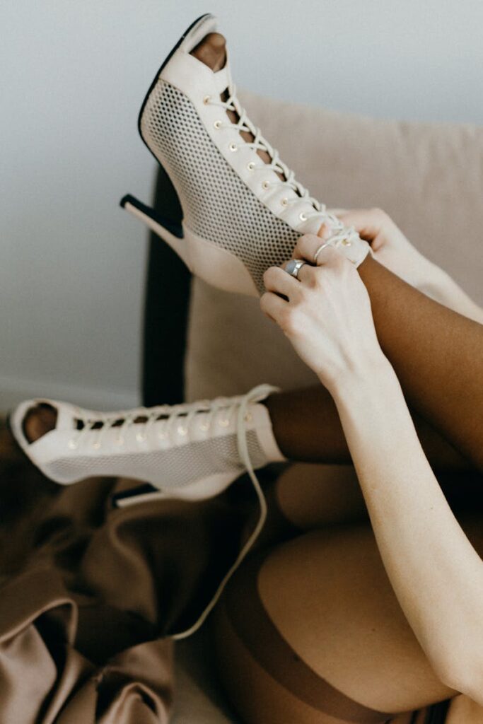 Faceless model lacing up beige stiletto heels with mesh design, emphasizing elegance and style.