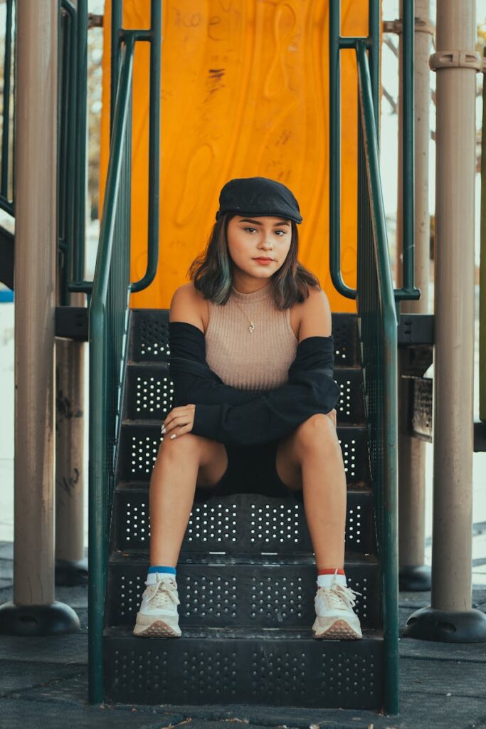 Portrait of a young woman in a flat cap sitting on playground stairs outdoors.