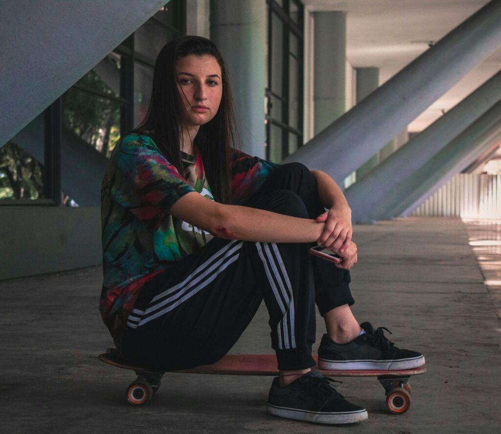 Young woman sitting on skateboard in modern indoor setting, casual and stylish.