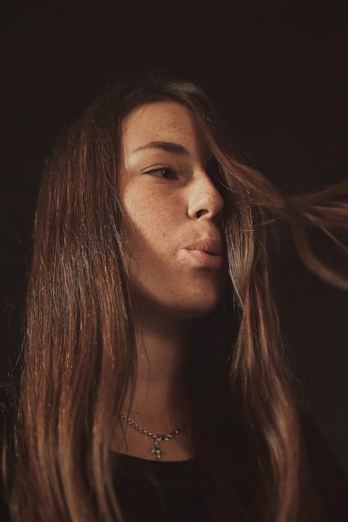 Close-up portrait of a young woman with freckles and flowing hair, captured in warm lighting.