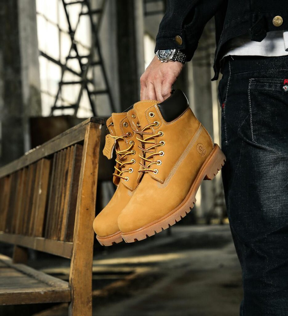 Close-up of fashionable brown hiking boots held by a man in an industrial environment.