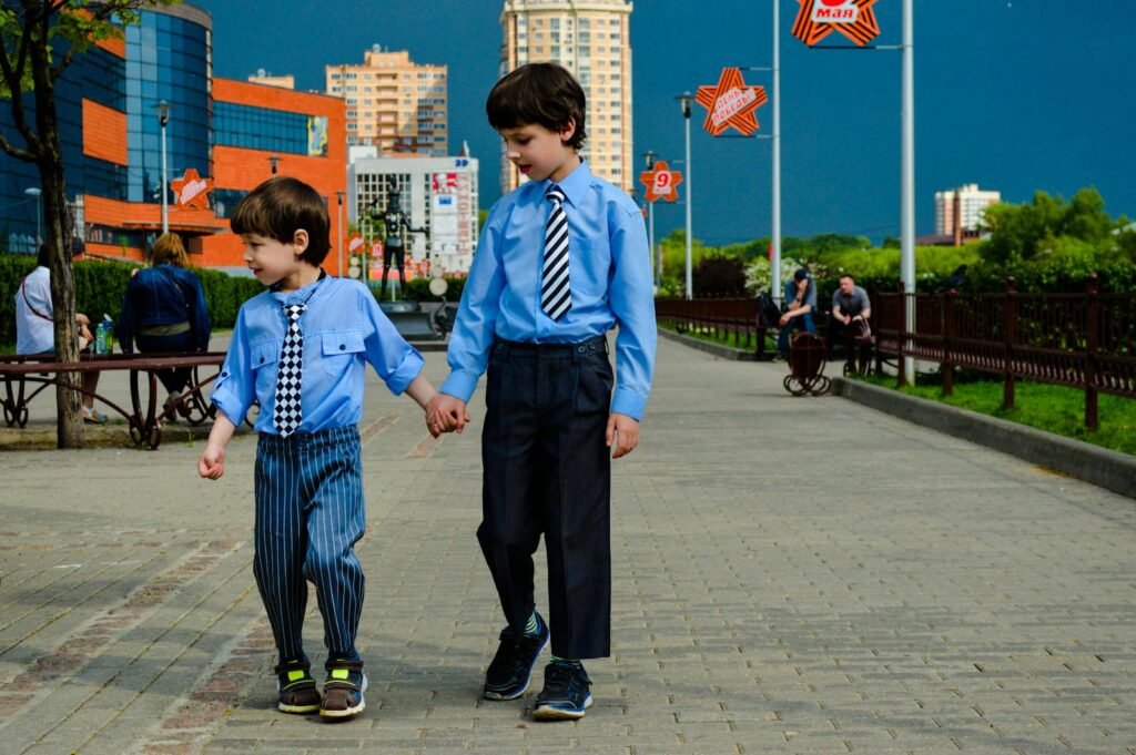 Two young boys in blue shirts holding hands on a city walkway.