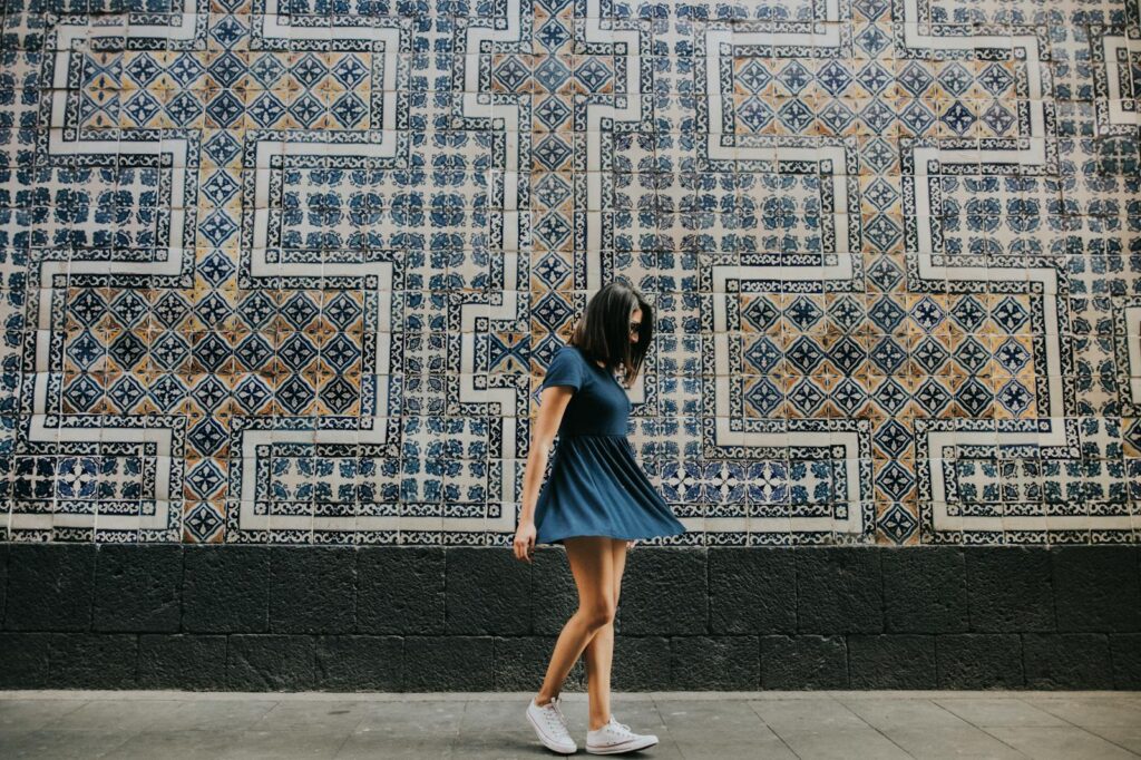 Woman in blue dress standing in front of a detailed mosaic wall with geometric patterns.