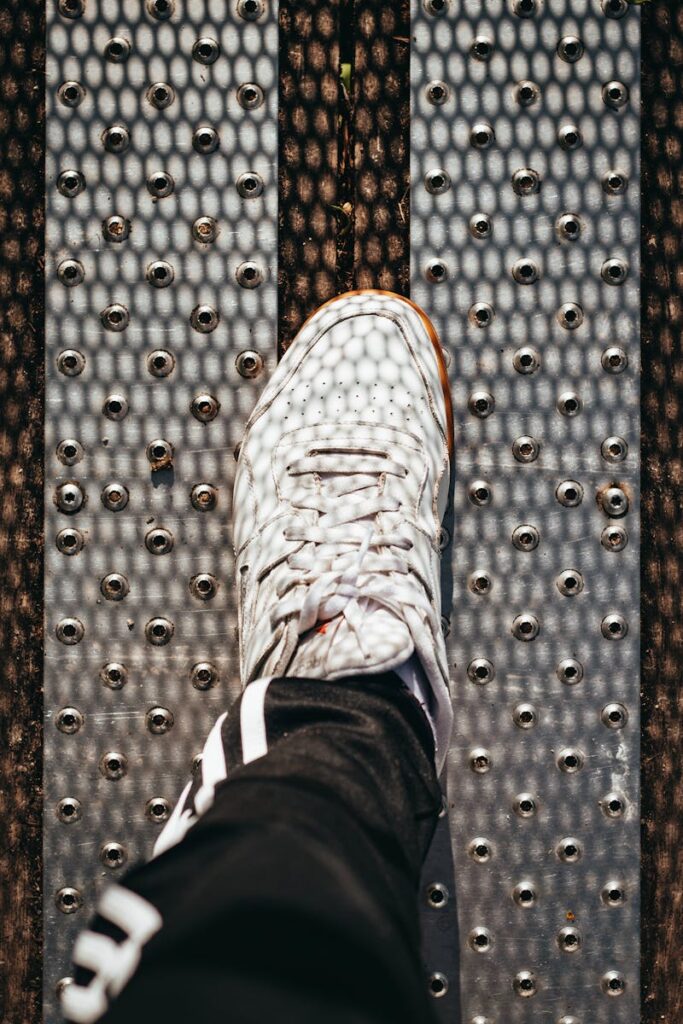 Foot in a white sneaker on a metallic patterned surface outdoors.