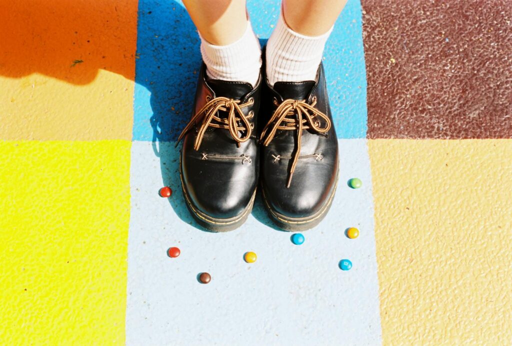 Black leather shoes on a colorful painted floor with candies. High-angle shot.