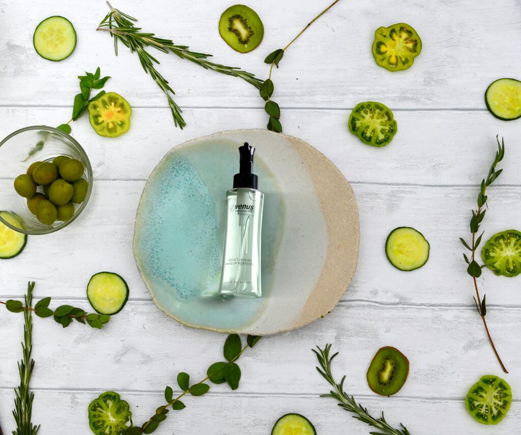 Flat lay of a natural skincare serum surrounded by fresh cucumber slices and herbs on a wooden table.
