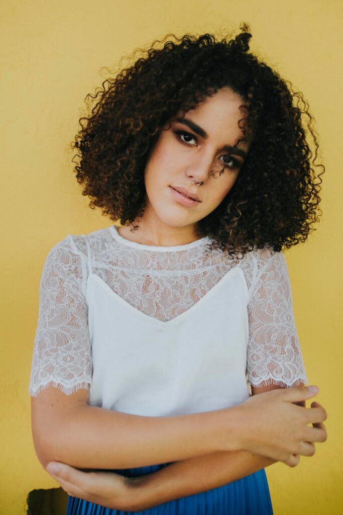 Young woman with curly hair posing against a vibrant yellow background.