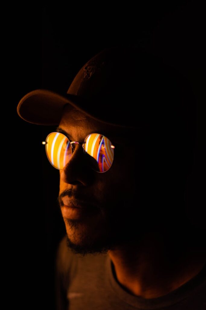 Stylish portrait of a man wearing reflective sunglasses in a dark setting, showcasing a unique artistic light reflection.