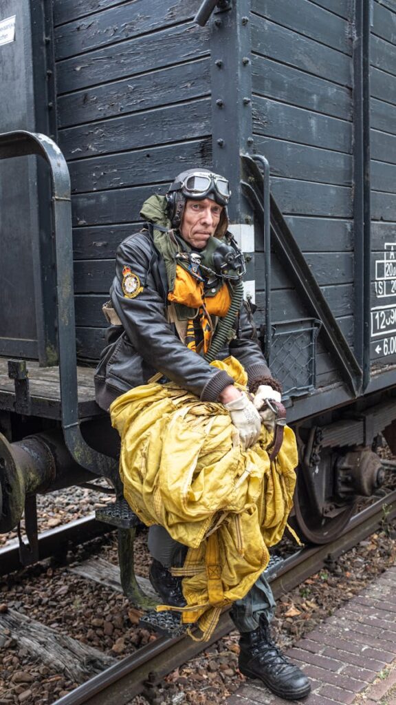 A World War II reenactor sits with parachute gear beside a vintage train.