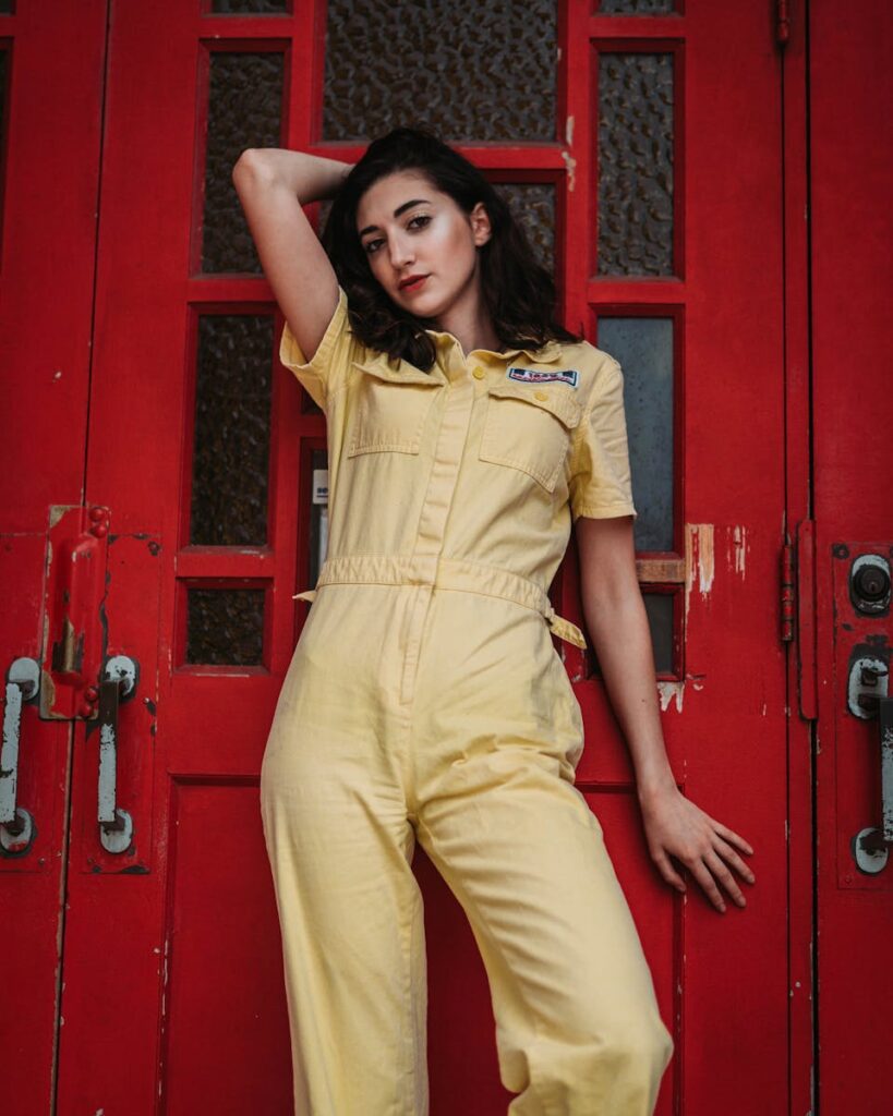 Portrait of stylish woman in a yellow jumpsuit leaning on a vibrant red door.