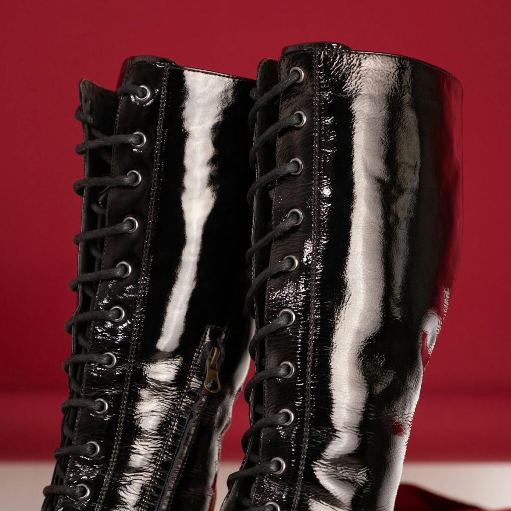 Close-up of shiny black patent leather boots with laces against a red background.