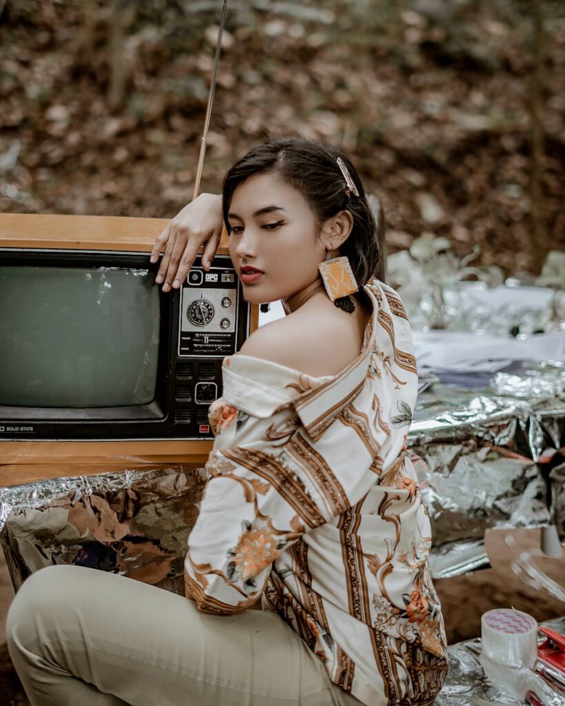 Stylish woman posing with a vintage TV in a retro-themed outdoor photoshoot.