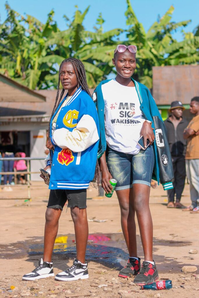 Two young women in varsity jackets enjoying a sunny day at an outdoor market.