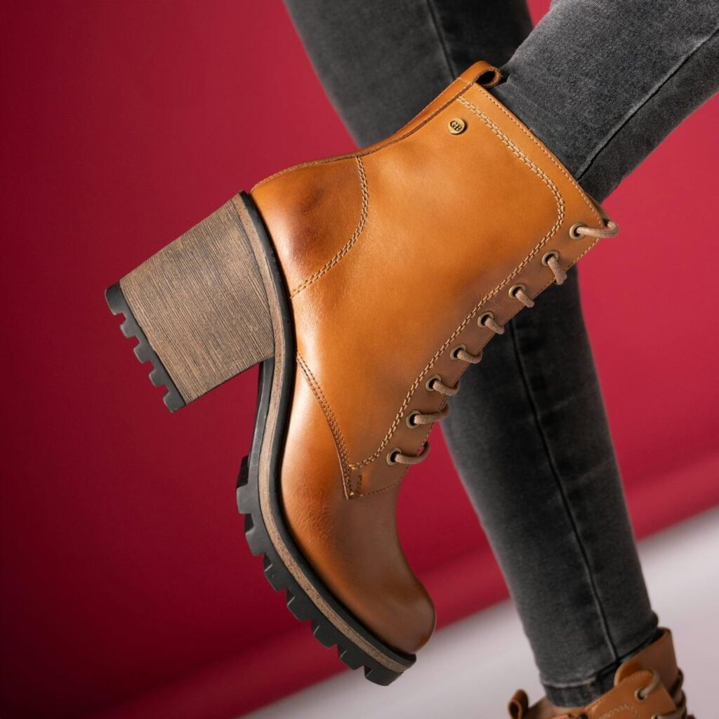 Close-up of fashionable tan leather ankle boot with chunky heel on red background.