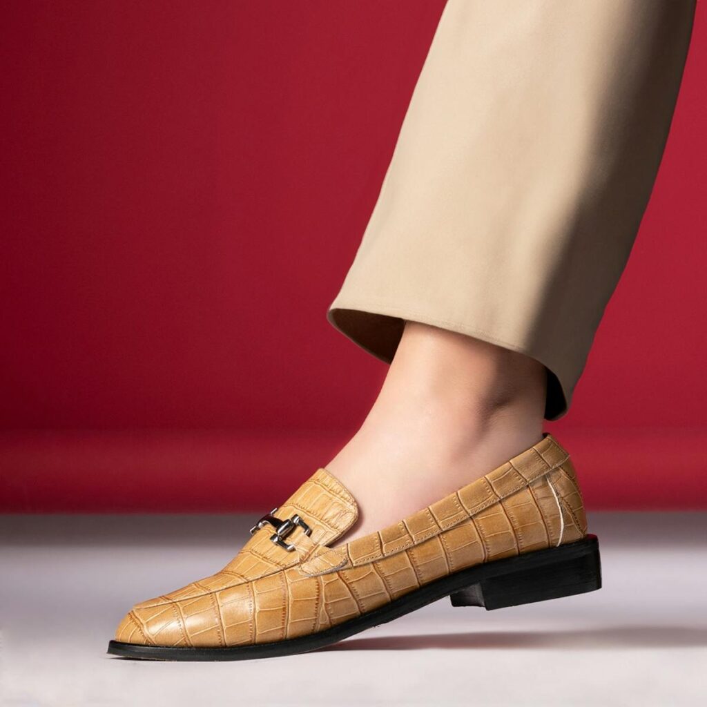 Stylish tan leather loafer with textured design on a vibrant red backdrop.