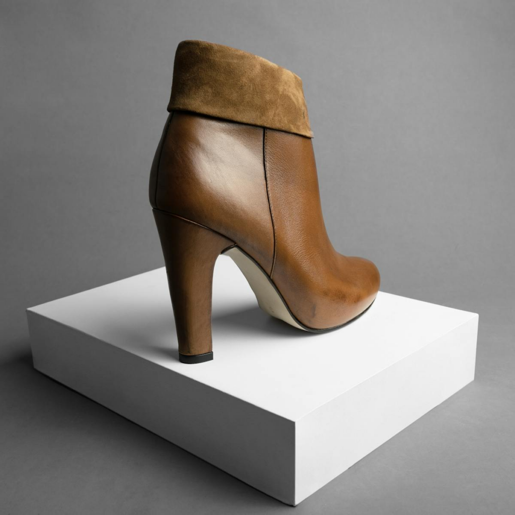 Stylish leather high-heeled ankle boot displayed on a minimalistic white stand.