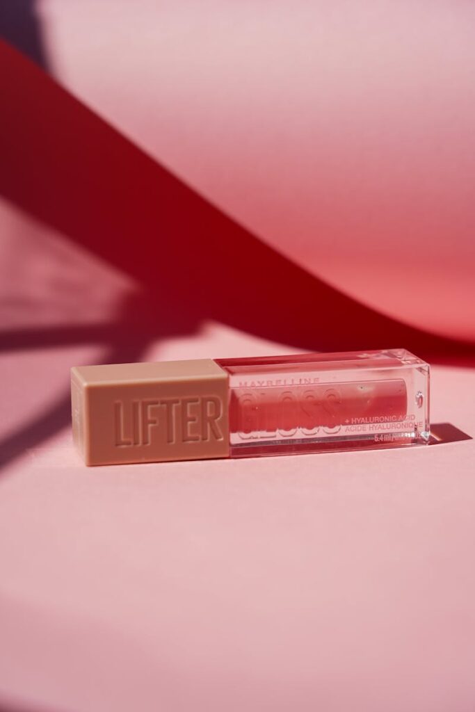 Elegant lip gloss tube with modern design on a pink backdrop, highlighting beauty.